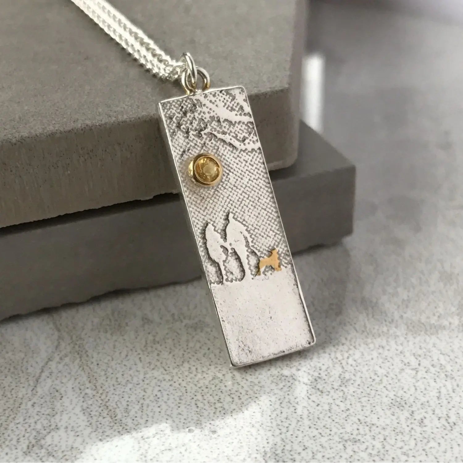 Dog lovers necklace featuring a couple and their dog beneath a yellow sapphire sun, displayed on a slate background.