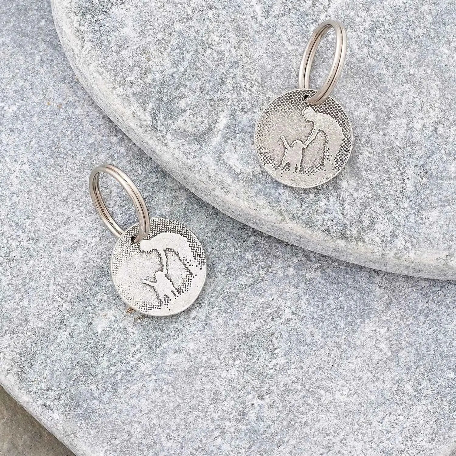 Personalised dog ID tags laid flat on a natural stone background.