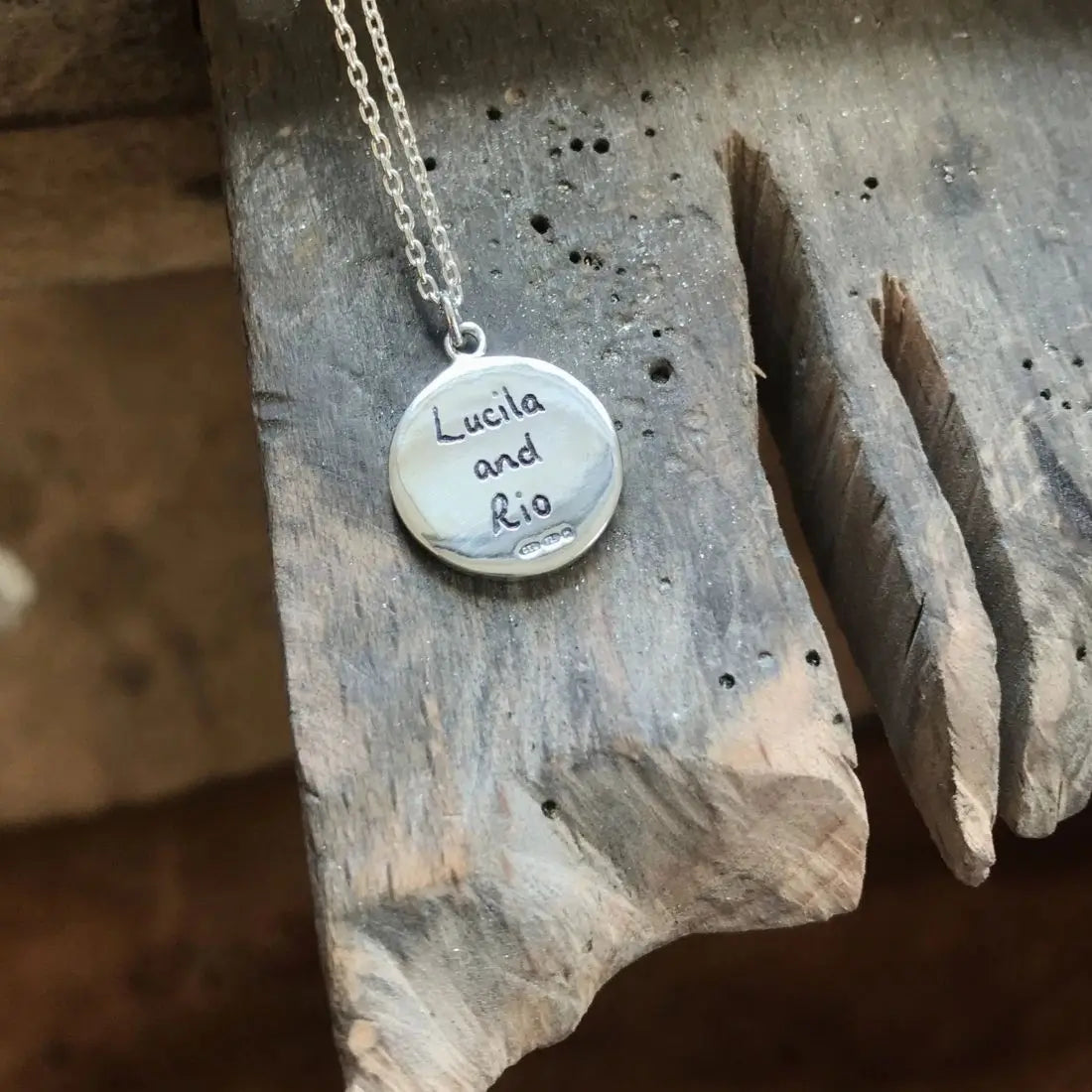Personalised engraving on the back of a round silver necklace with personalised engraving that reads 'Lucila and Rio'.
