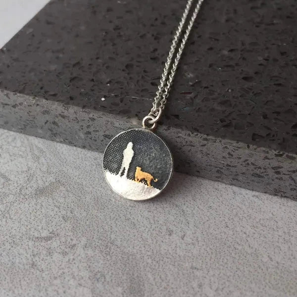 Walks Under Night’s Sky Gold Dog Necklace shown in a lifestyle setting on a grey textured background with sterling silver round pendant and gold‑vermeil dog detail.