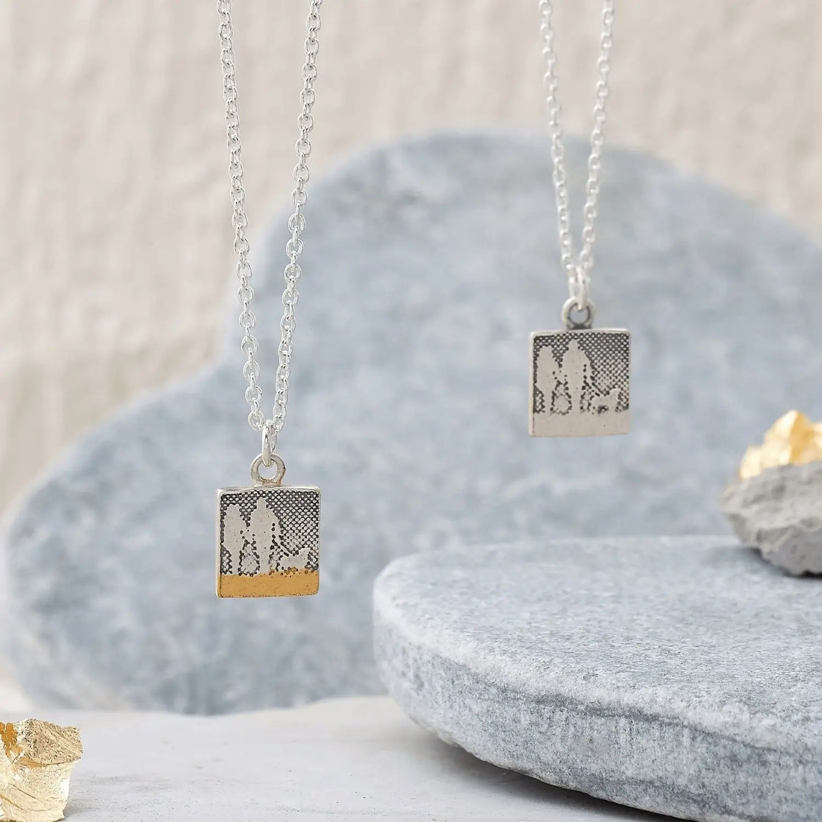 Small sterling silver couple and dog necklaces displayed on a natural background, showing the etched silhouette artwork.