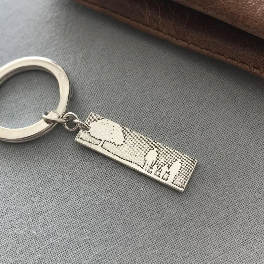 Sterling silver family tree keyring on grey material next to wallet.