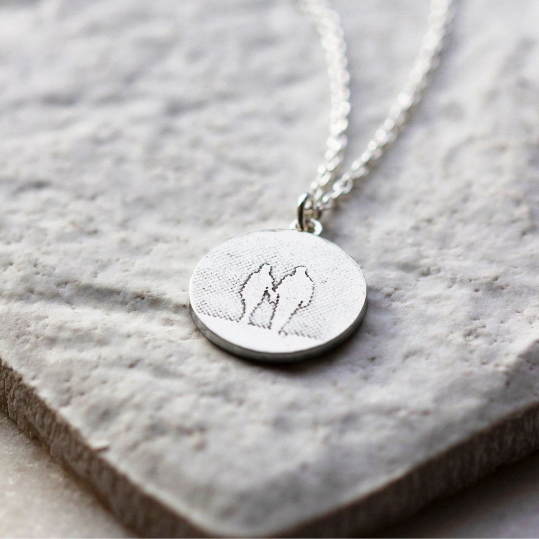 Round Silver Couple Necklace displayed on a natural background, showing the etched silhouette and polished silver finish.