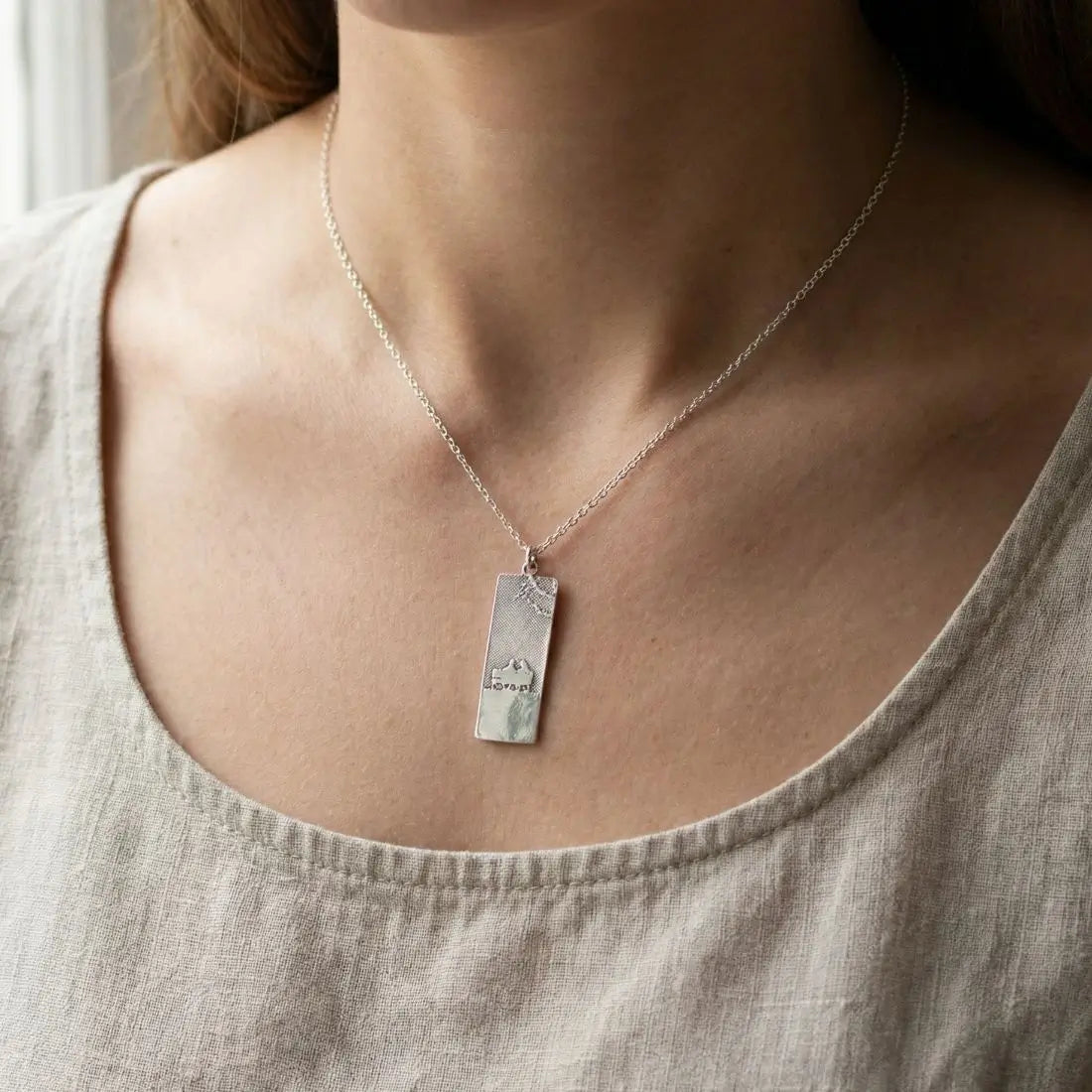 Always with you memory necklace worn by model featuring  etched image of two figures on a bench.