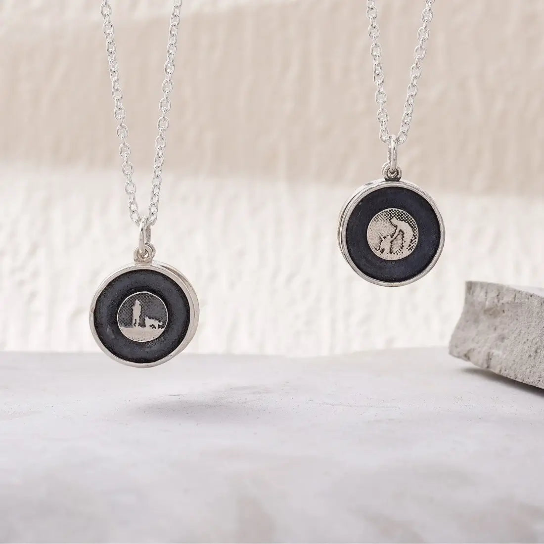Two sterling silver dog lovers lockets shown closed, featuring petting and standing silhouettes with silver and black sky finishes.