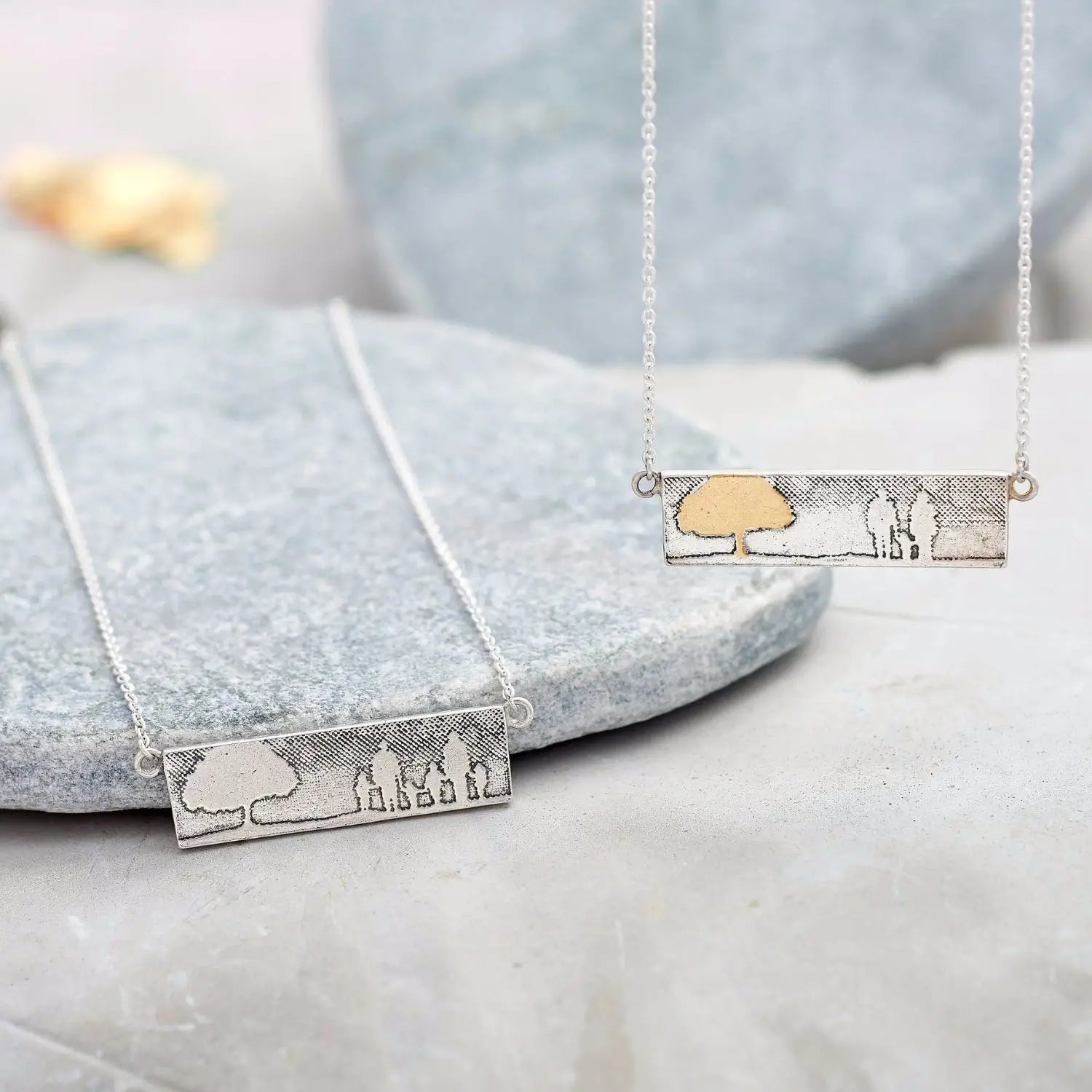 Sterling silver landscape family necklace with 22ct gold vermeil tree next to silver family tree necklace.