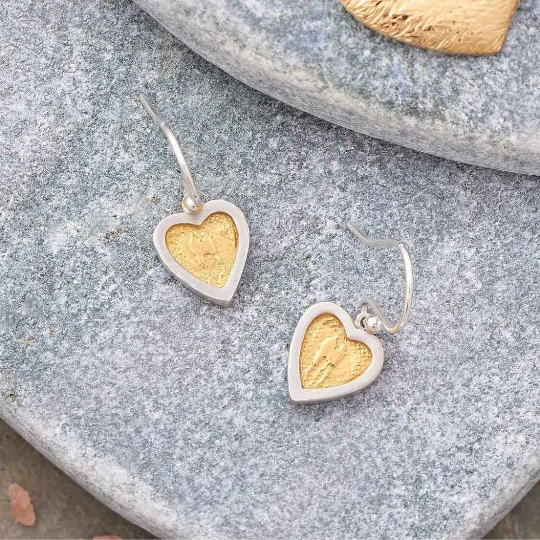 Heart earrings with golden centre lay flat on stone background.