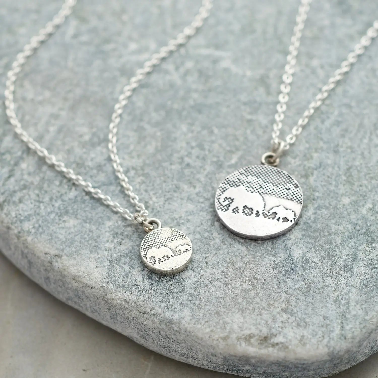 Flatlay image of mother and baby elephant necklace and small version of necklace in sterling silver.