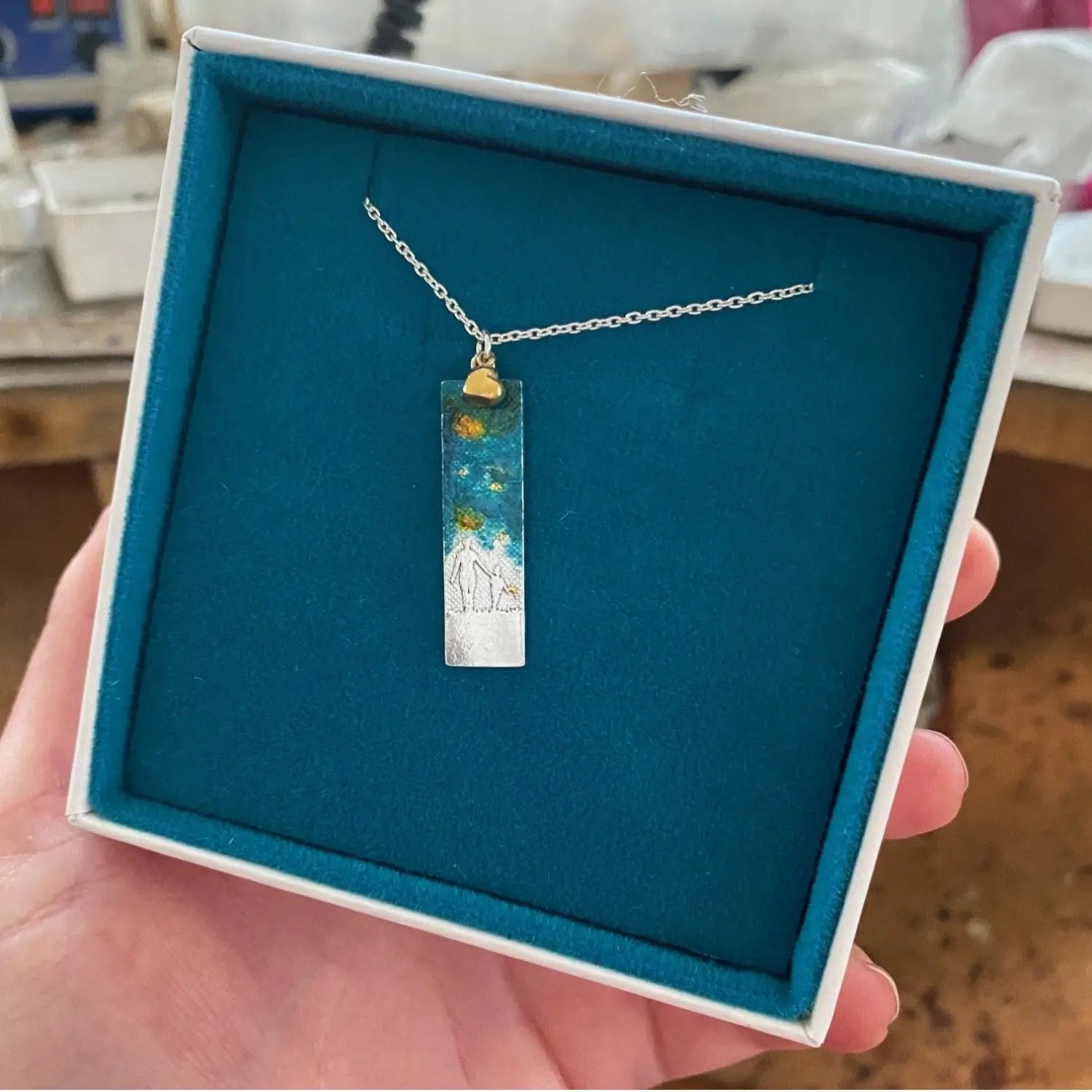 mother and child rectangle necklace with golden details in blue and white packaging.