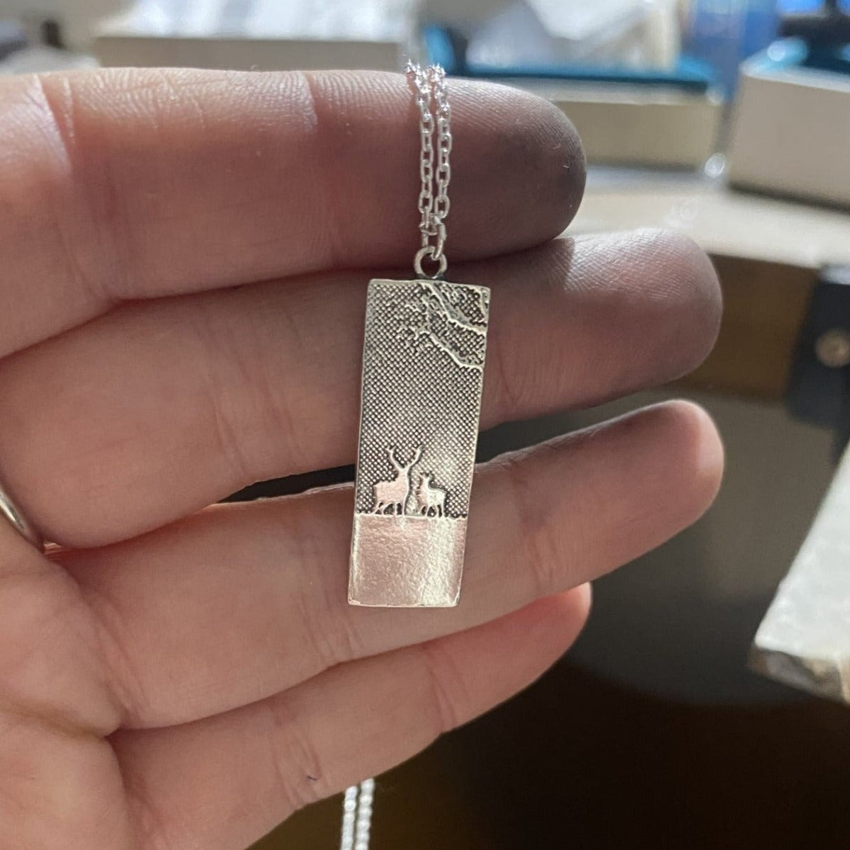 Maker holding the sterling silver my dear deer necklace with etched silhouette of two deers in their hand.