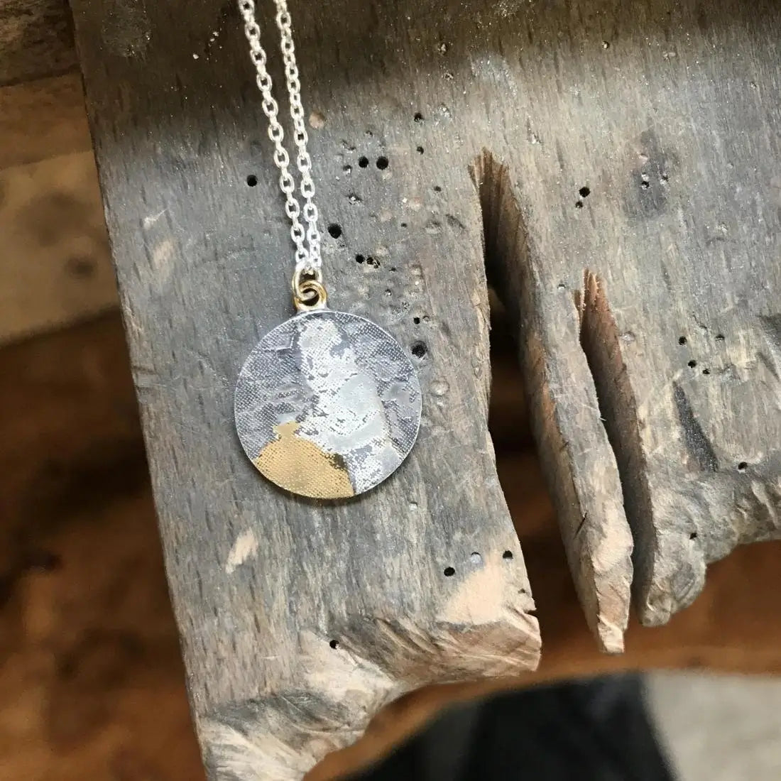 Personalised silver photo memory necklace with golden detail laid out on jewellers bench peg.