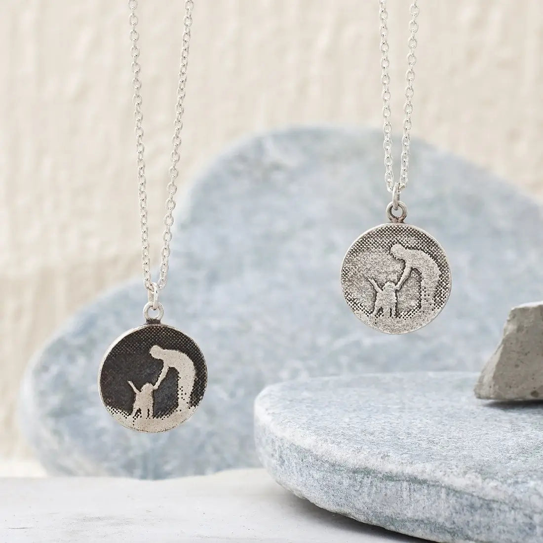 Two round sterling silver dog necklaces hanging side by side, showing the silver sky and black oxidised sky finishes with etched petting silhouettes.