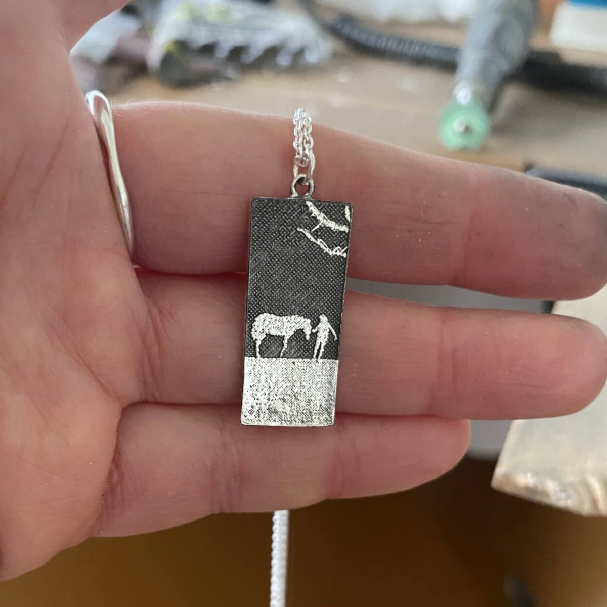 Maker holding the horse lovers necklace with oxidised silver nights sky finish with polished silver horse and owner.