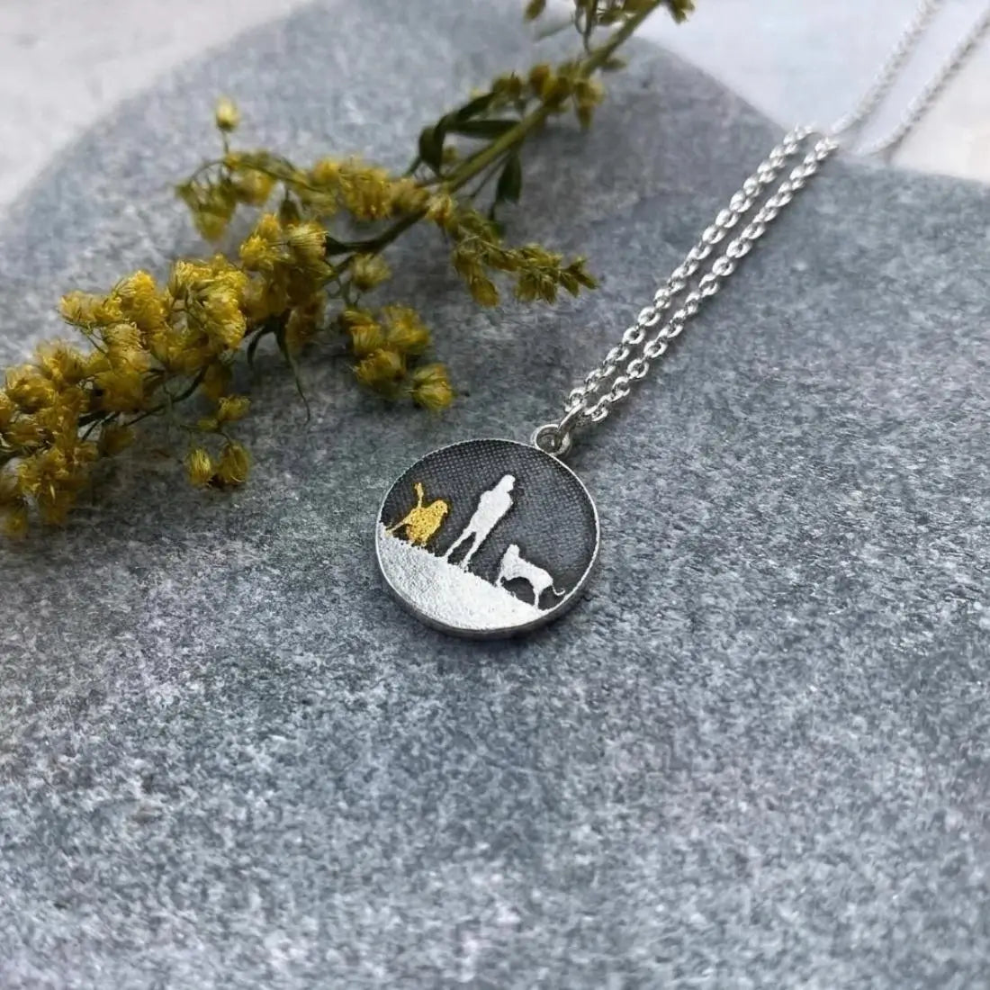 Two Dogs Night’s Sky Necklace displayed on a natural background showing the etched person and two dogs silhouette.