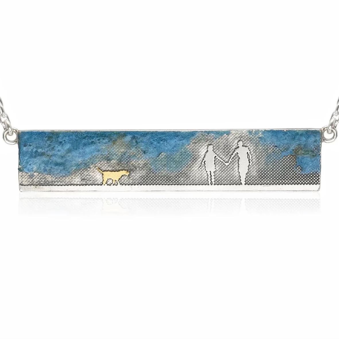 Sterling silver landscape necklace showing a couple walking with their dog in the countryside beneath a blue enamel sky.